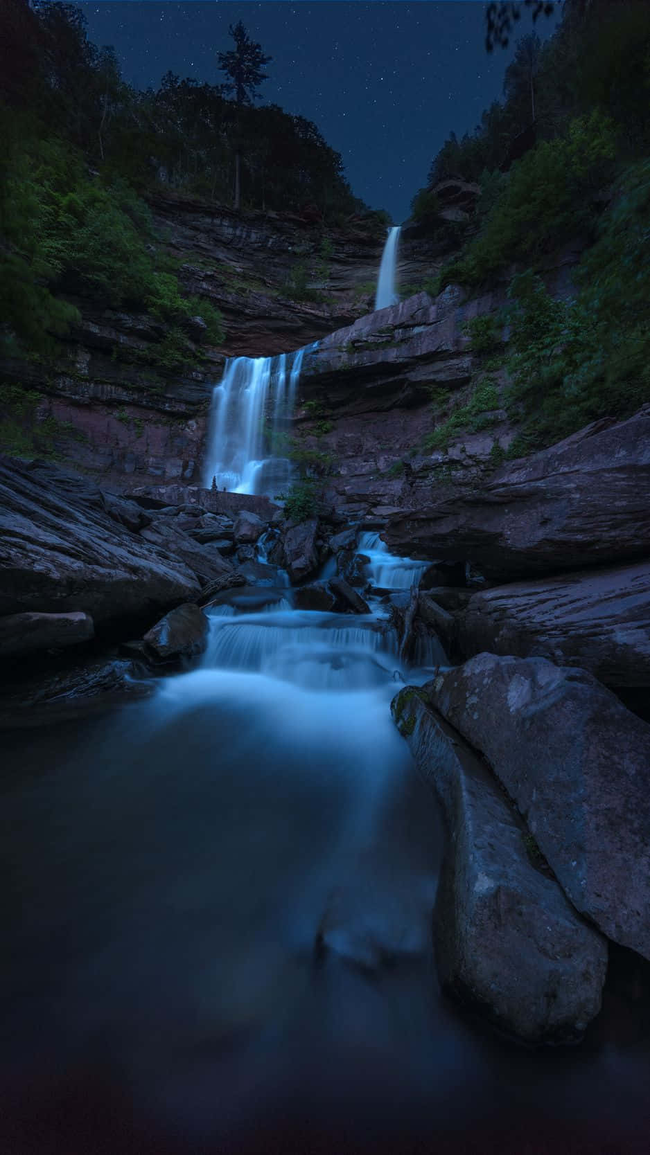 A Waterfall In The Dark With Stars Above It