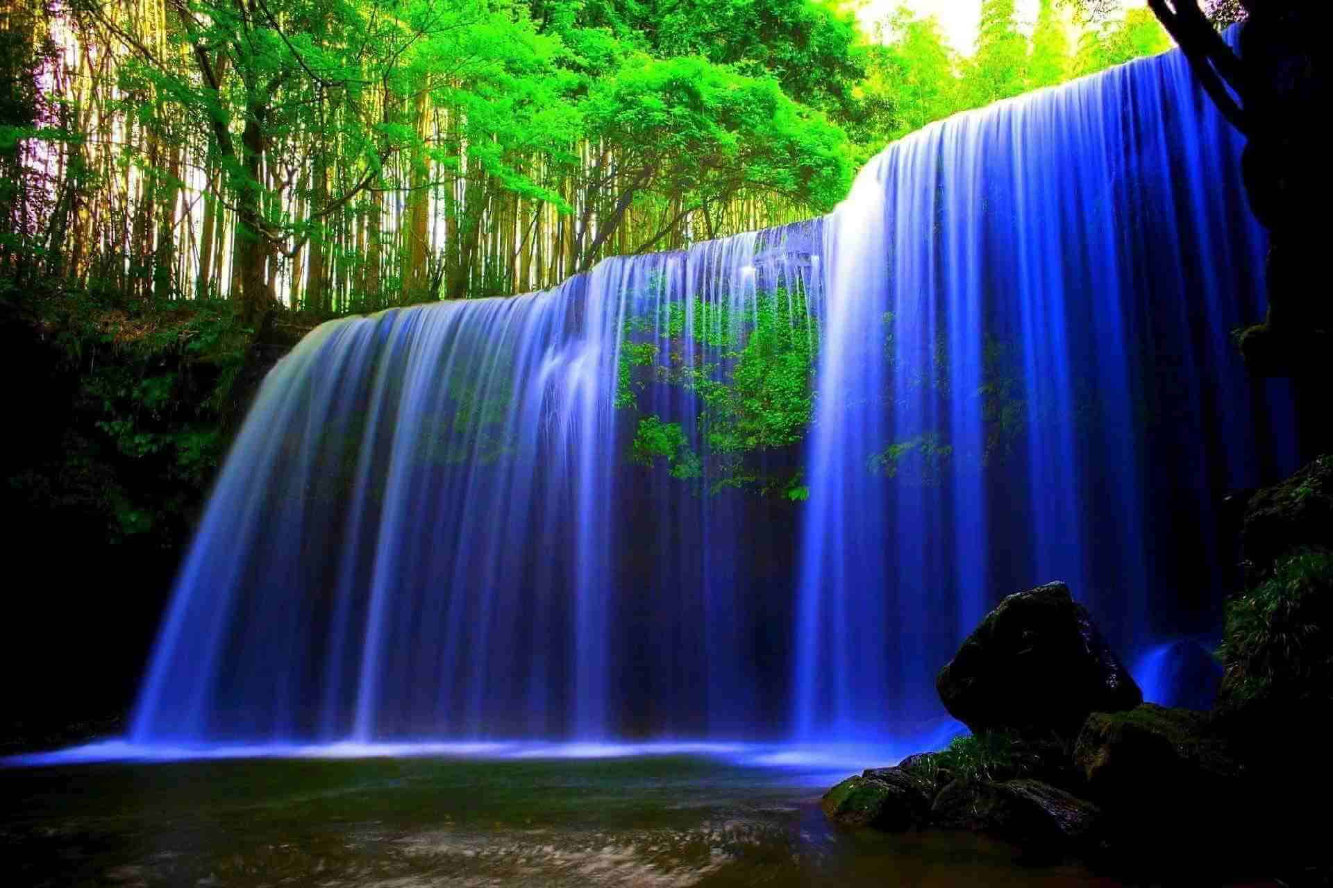 A Waterfall In The Forest With Blue Water Background