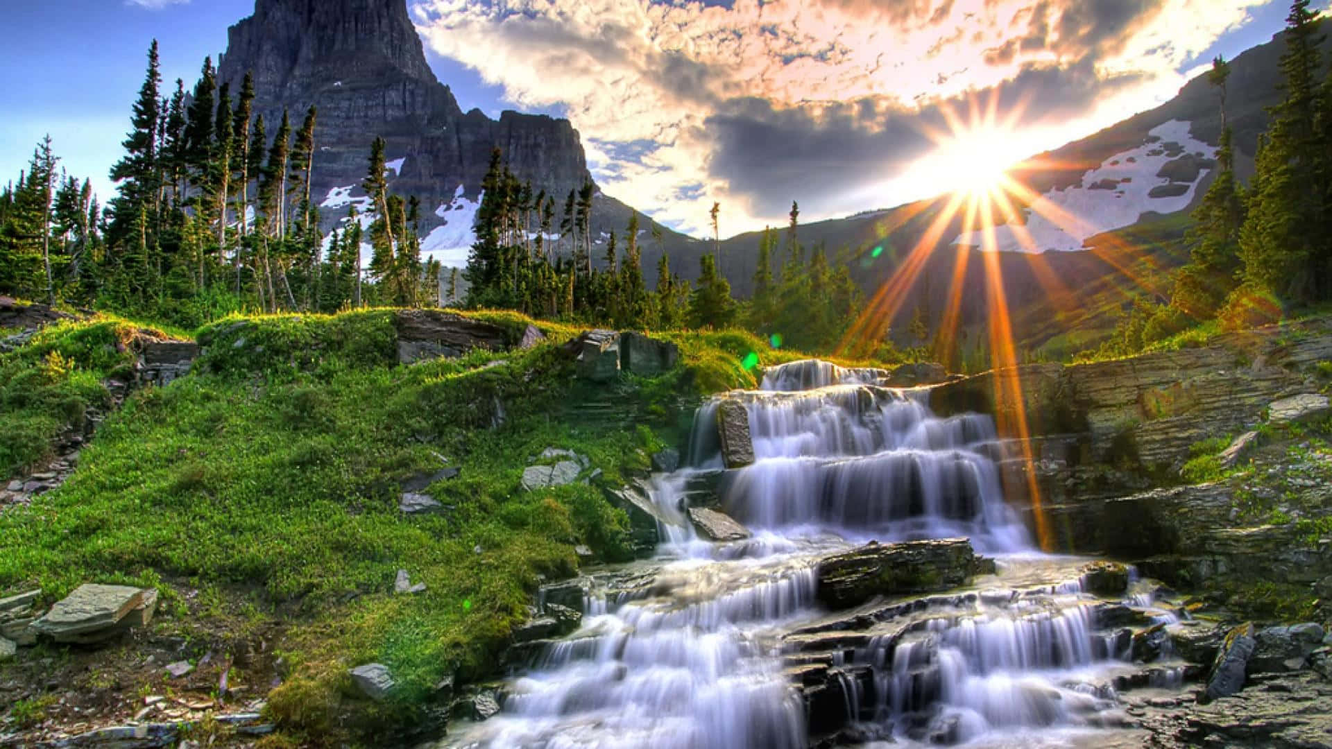 A Waterfall In The Mountains With The Sun Shining On It Background