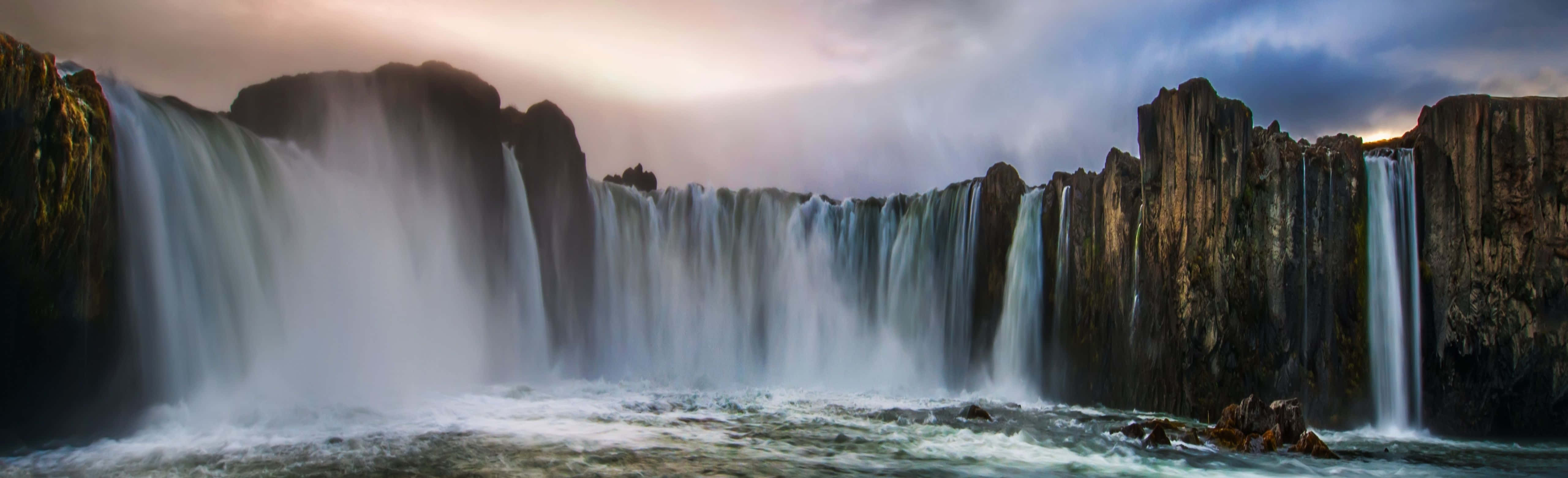 A Waterfall With A Cloudy Sky And Rocks