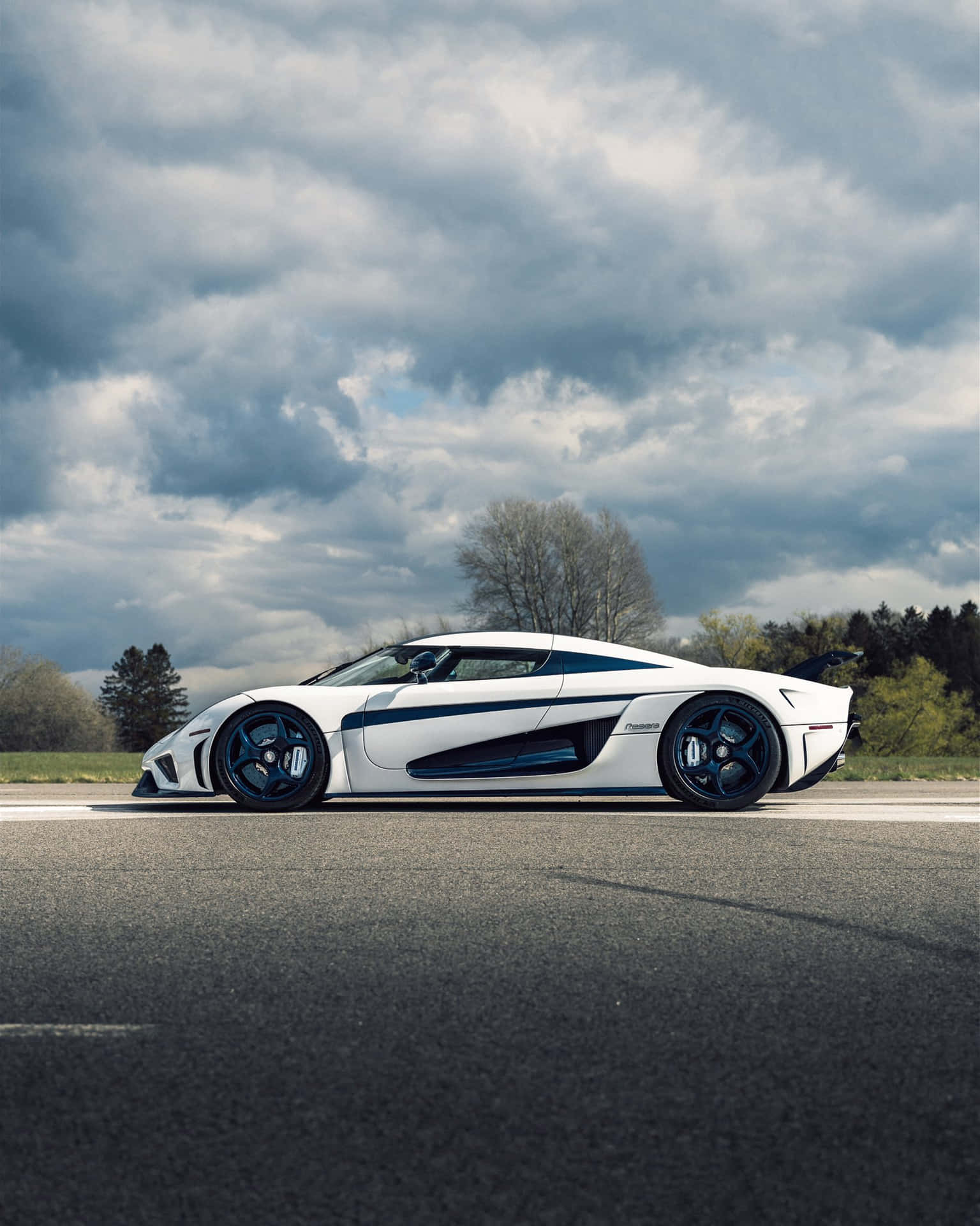 A White And Blue Sports Car Is Driving Down The Road Background