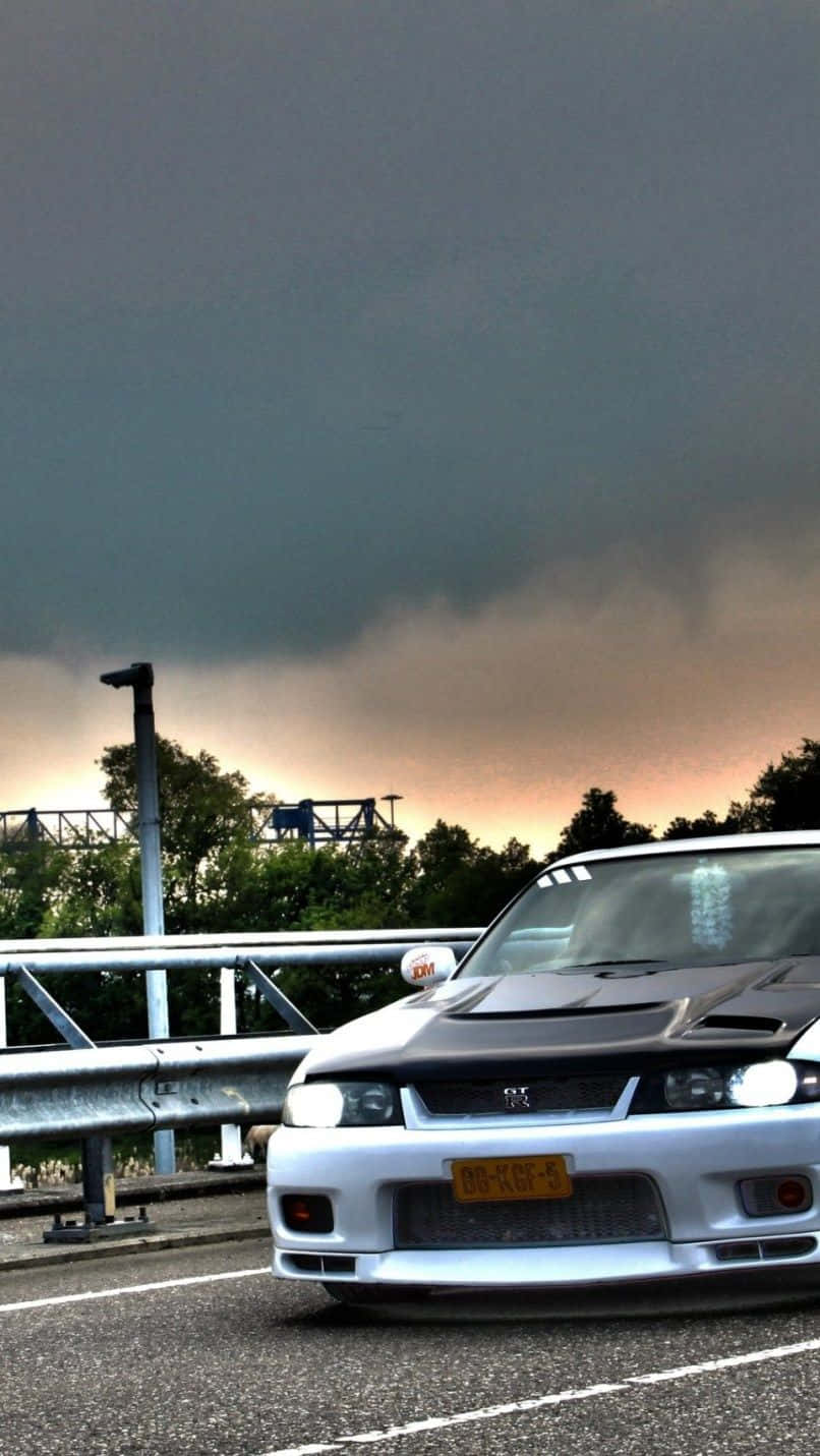 A White Car Driving On A Bridge Under A Cloudy Sky Background