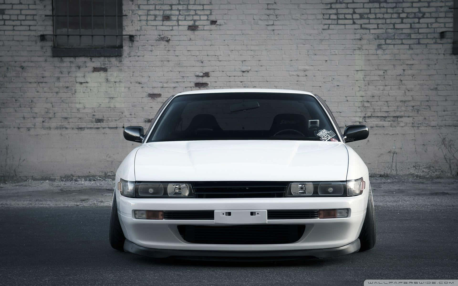 A White Car Parked In Front Of A Brick Wall Background