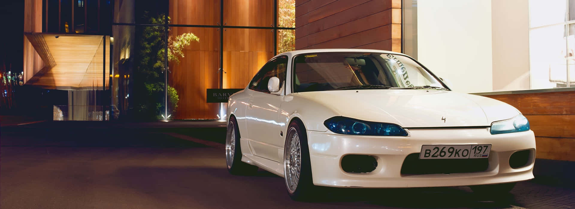 A White Car Parked In Front Of A Building At Night Background