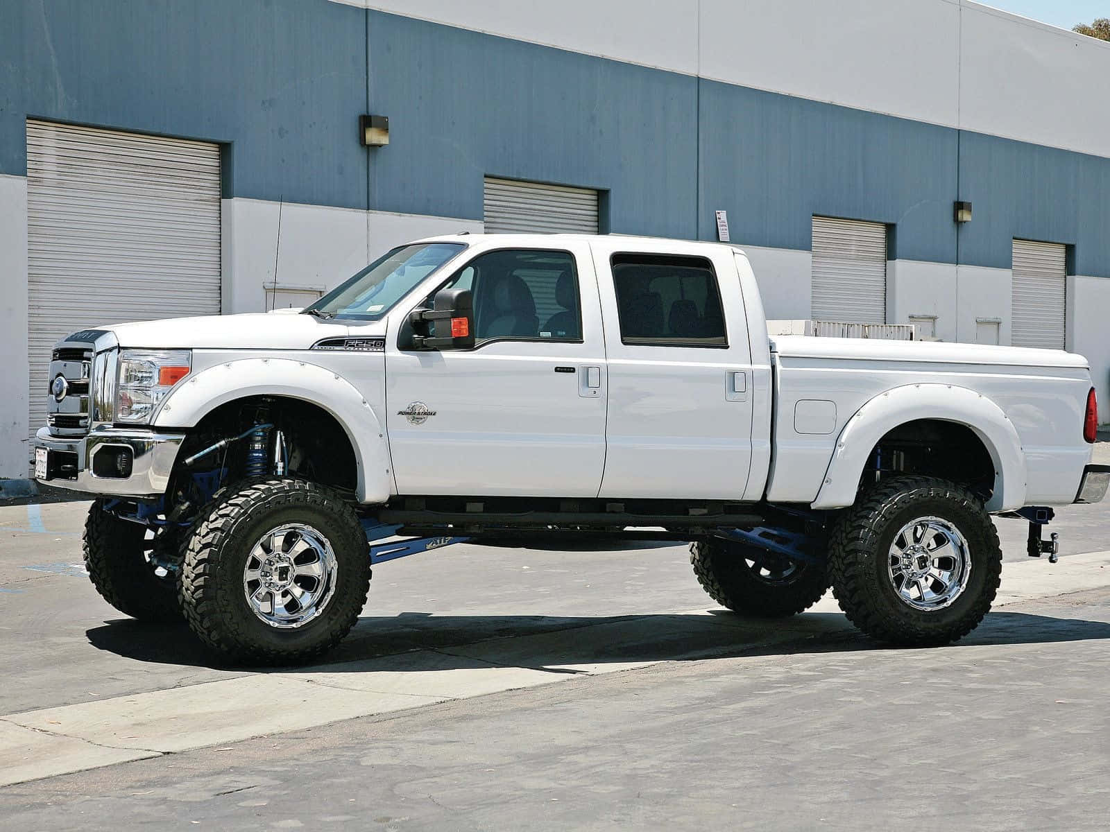 A White Ford F-250 Lifted Truck Parked In Front Of A Building Background