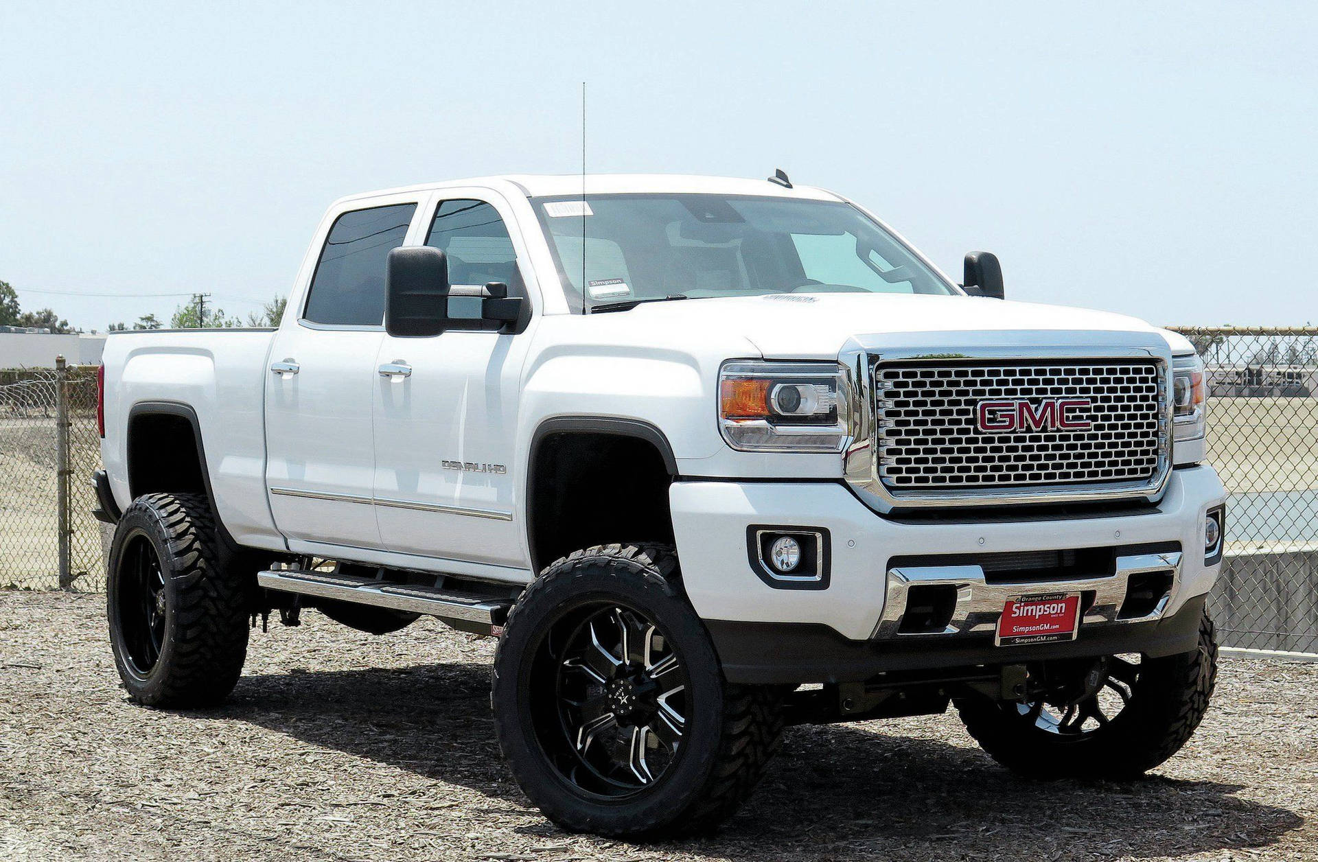 A White Gmc Sierra Truck Is Parked In A Dirt Lot