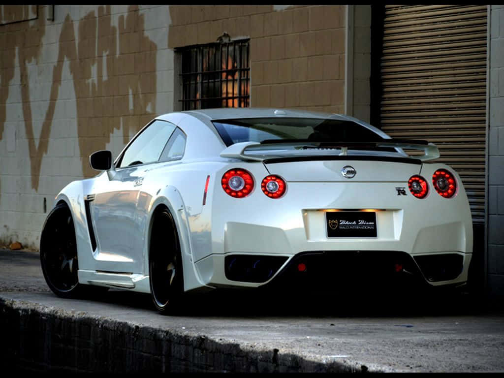 A White Nissan Gtr Parked In Front Of A Garage Background