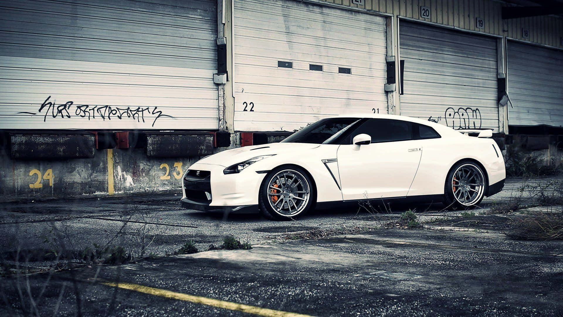 A White Nissan Gtr Parked In Front Of A Garage Background