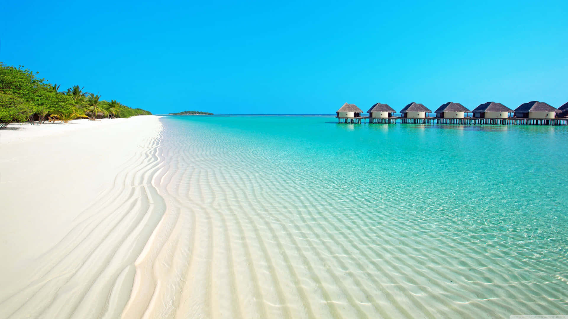 A White Sandy Beach With Huts And A Blue Ocean Background