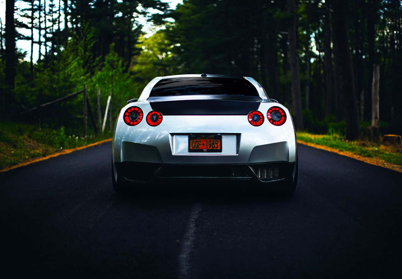 A White Sports Car Driving Down A Road In The Woods Background