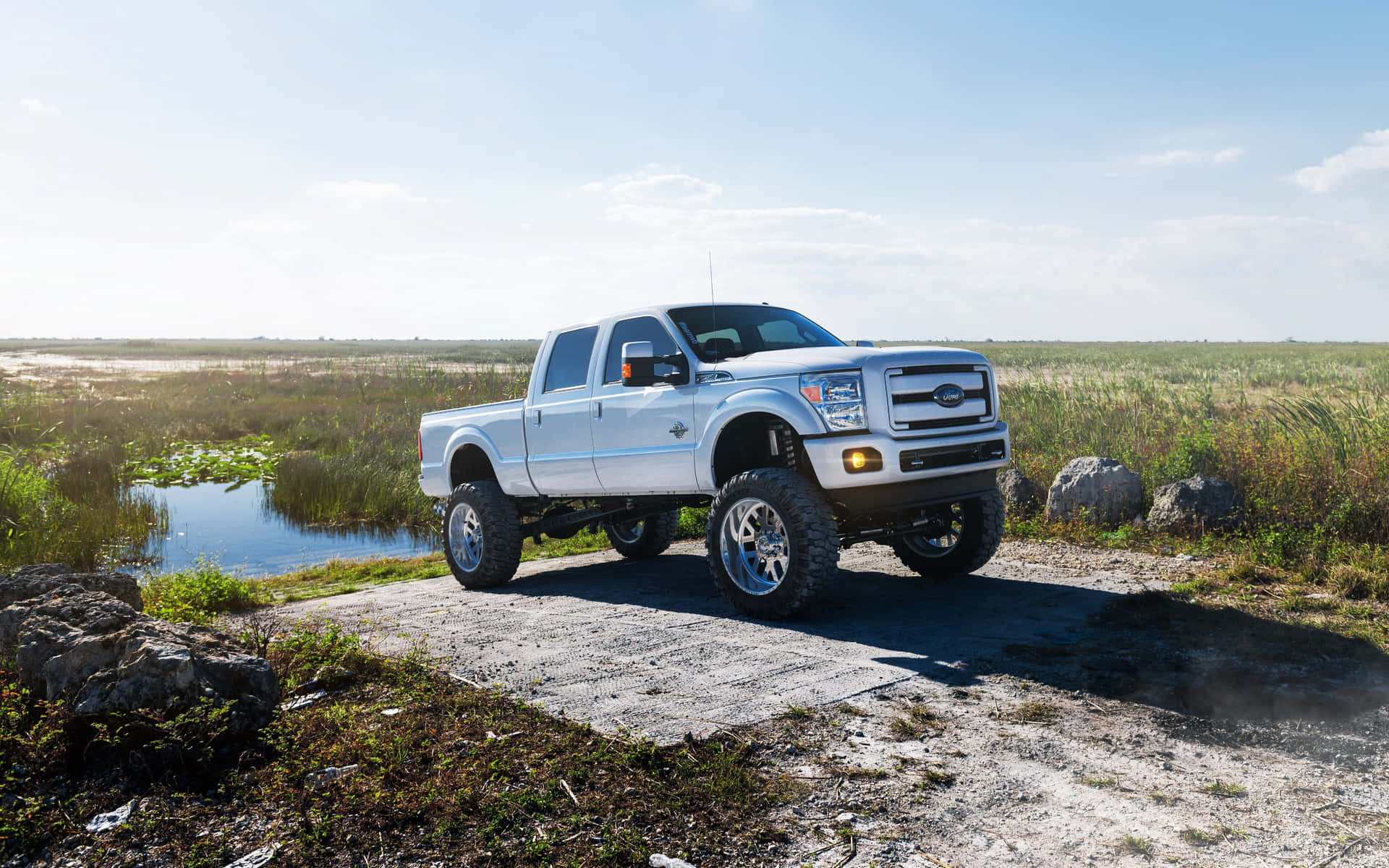 A White Truck Is Parked On A Dirt Road Near A Lake