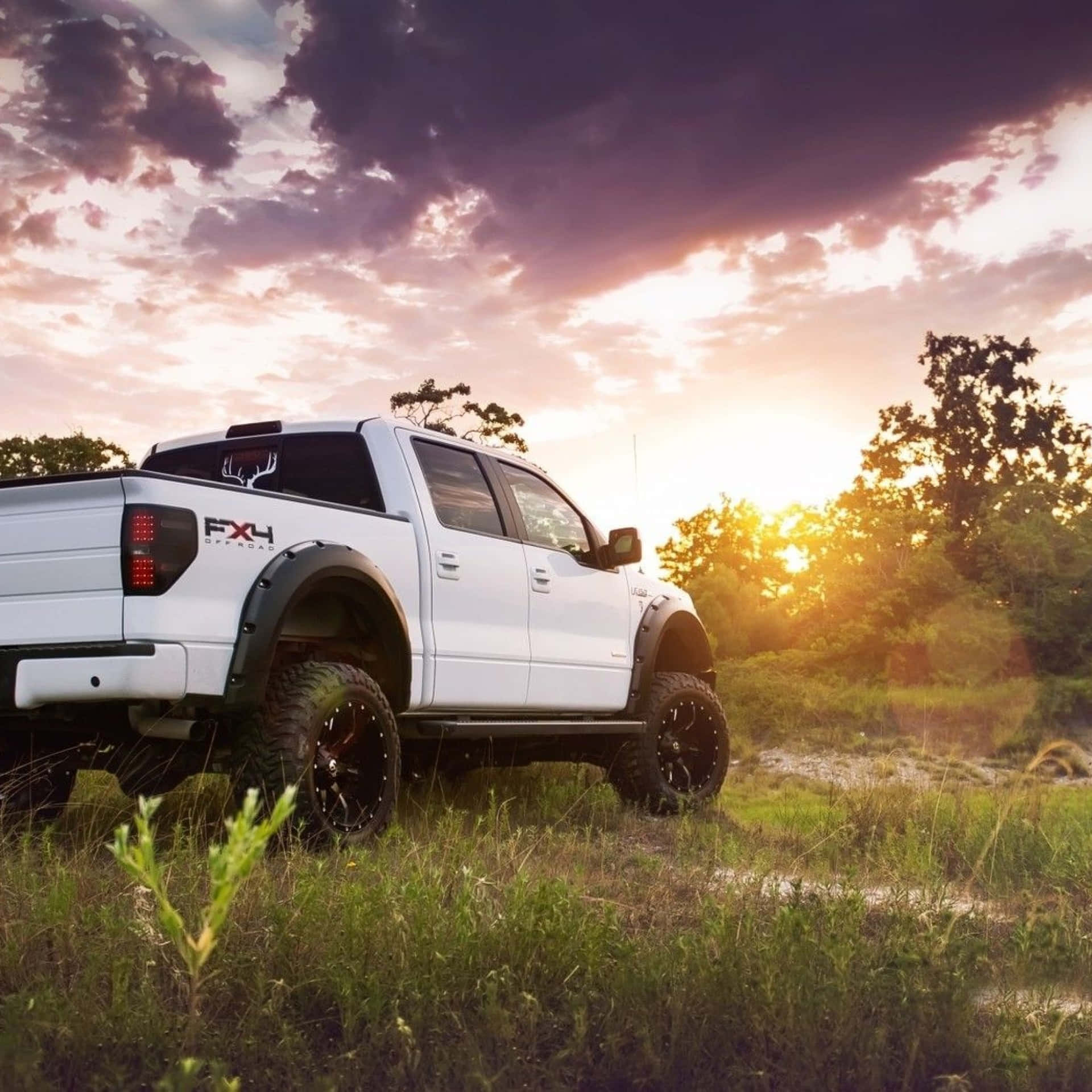 A White Truck Parked In A Field At Sunset Background