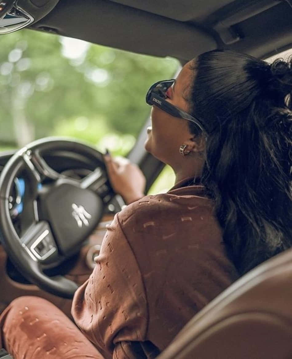 A Woman Driving A Car With Sunglasses On Background