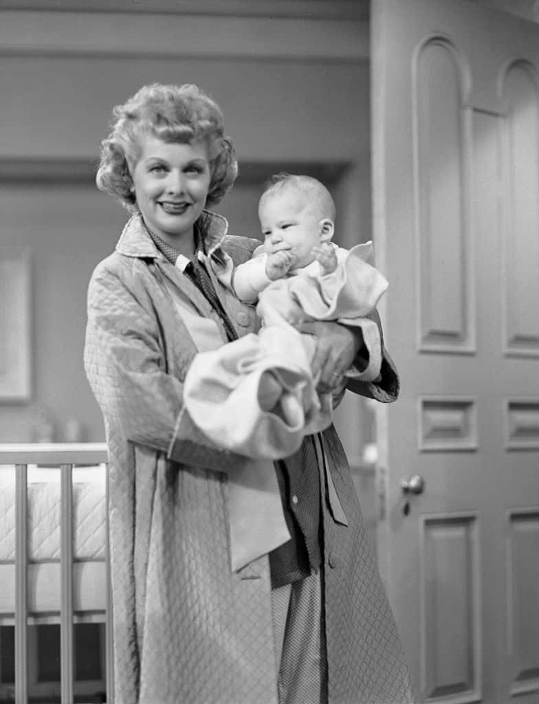 A Woman Holding A Baby In A Coat Background