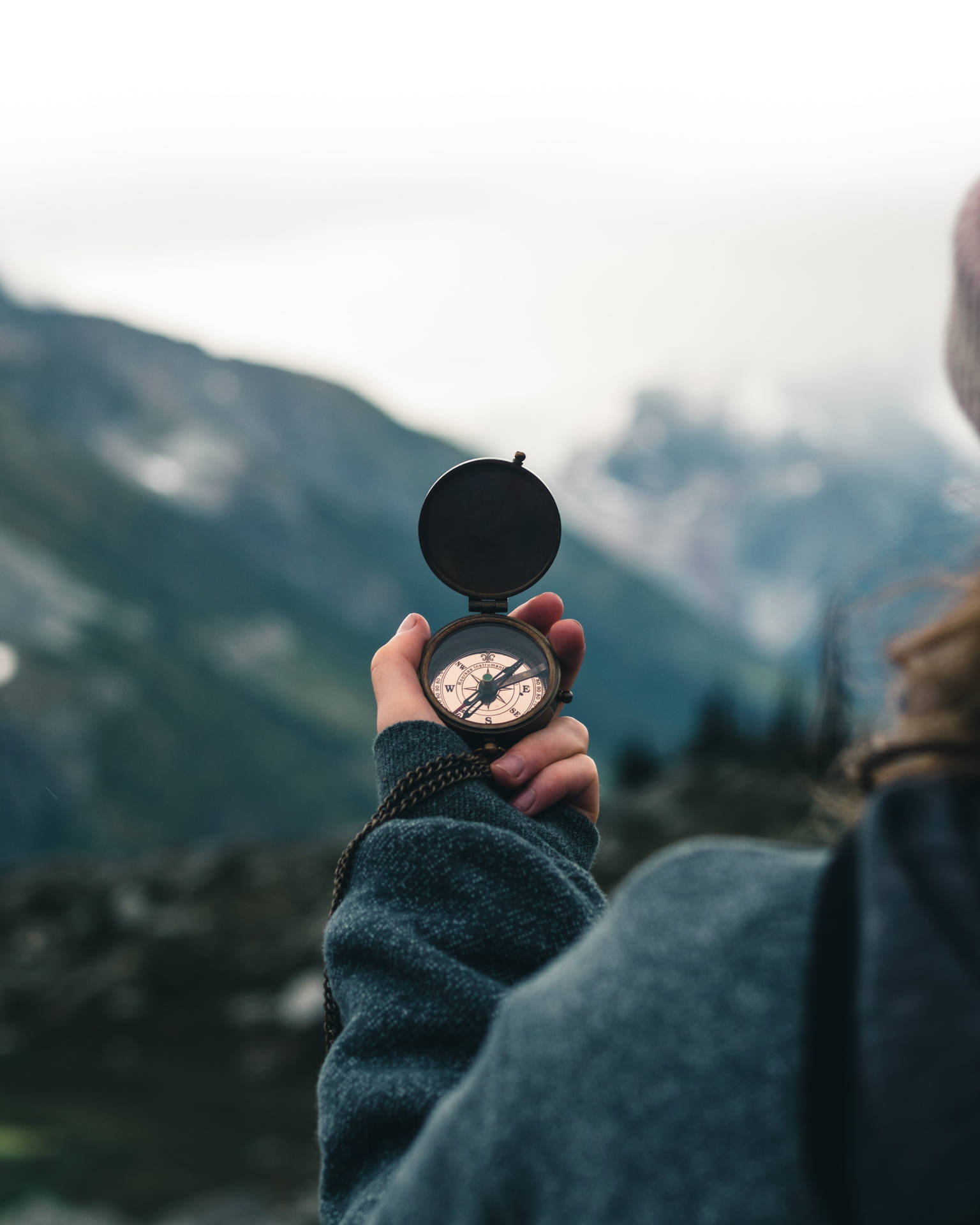 A Woman Holding A Compass In Front Of Mountains Background