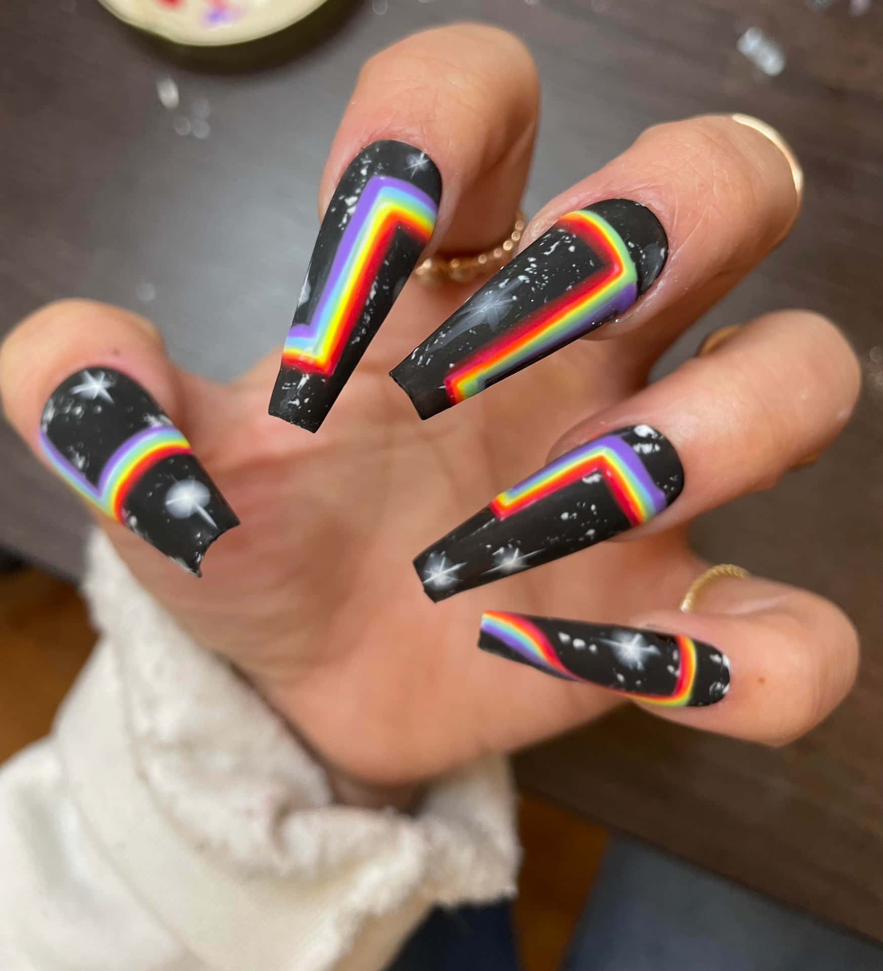 A Woman Holding Up A Black Nail With Rainbow Designs Background