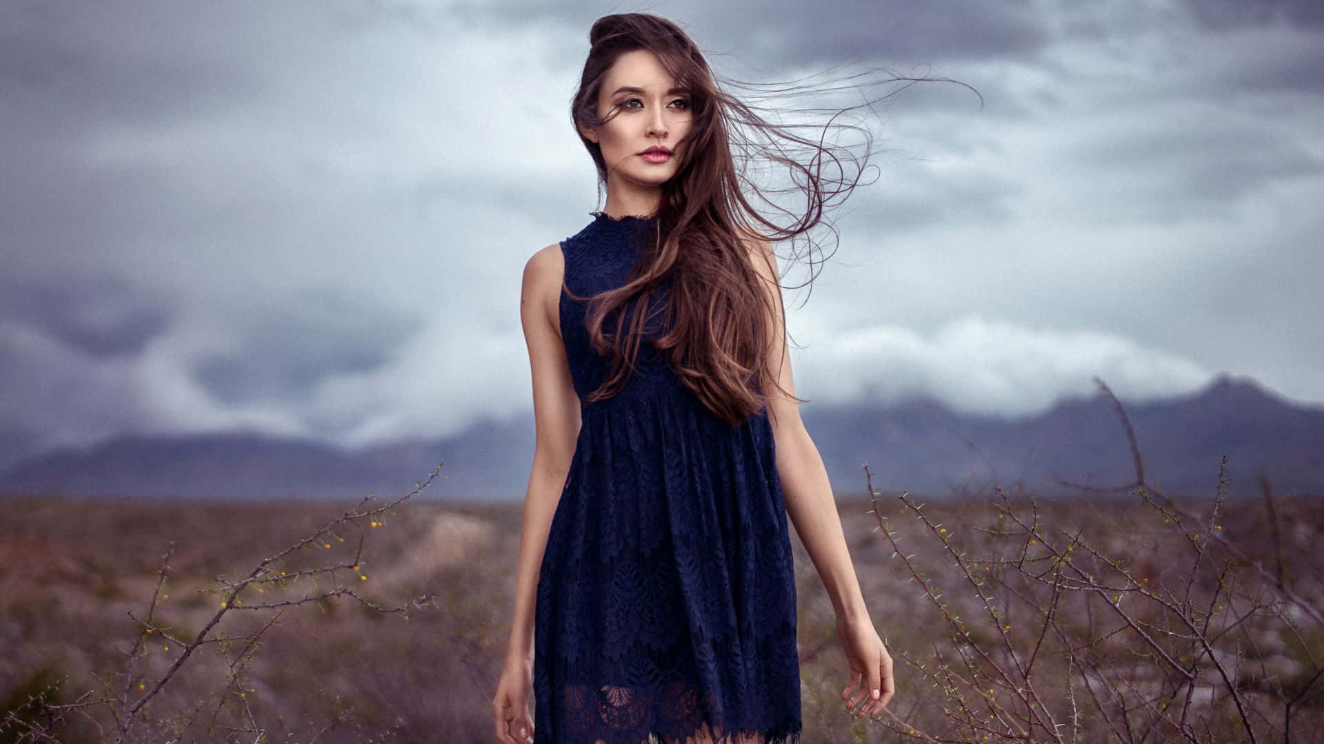 A Woman In A Blue Dress Standing In A Field Background