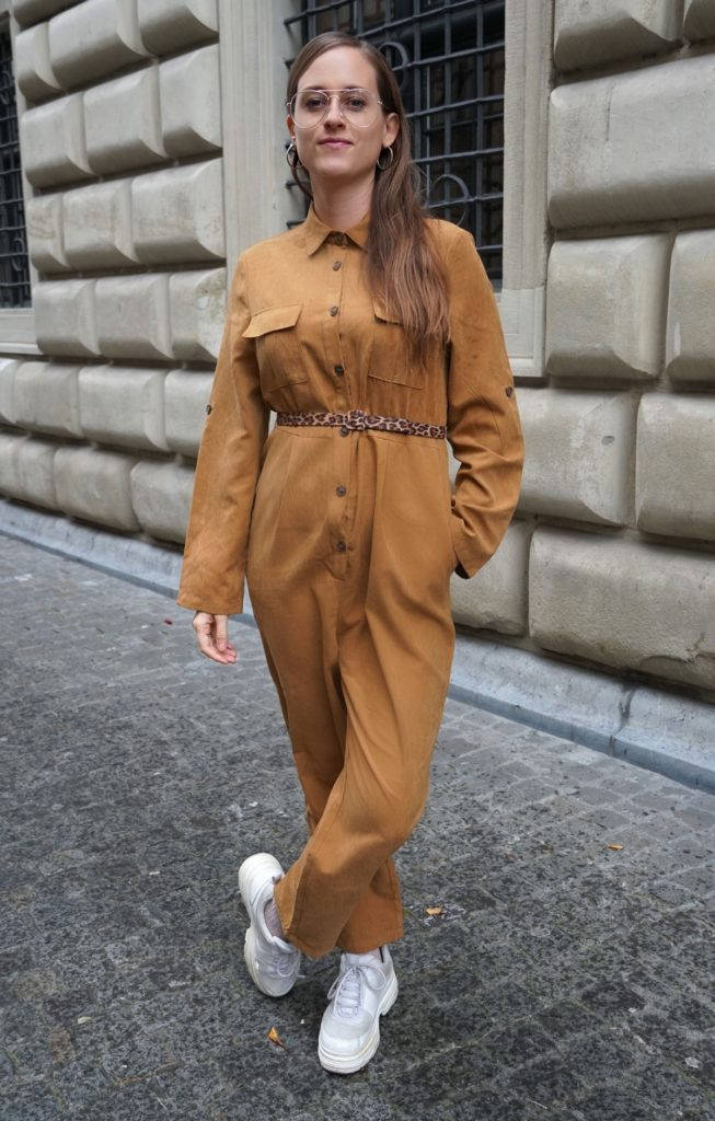 A Woman In A Brown Jumpsuit Standing On A Street