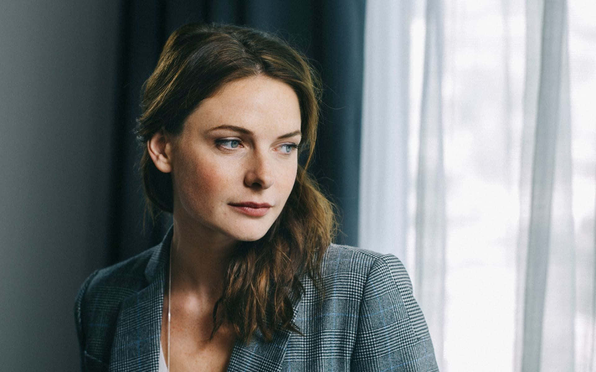 A Woman In A Gray Suit Looking Out The Window Background