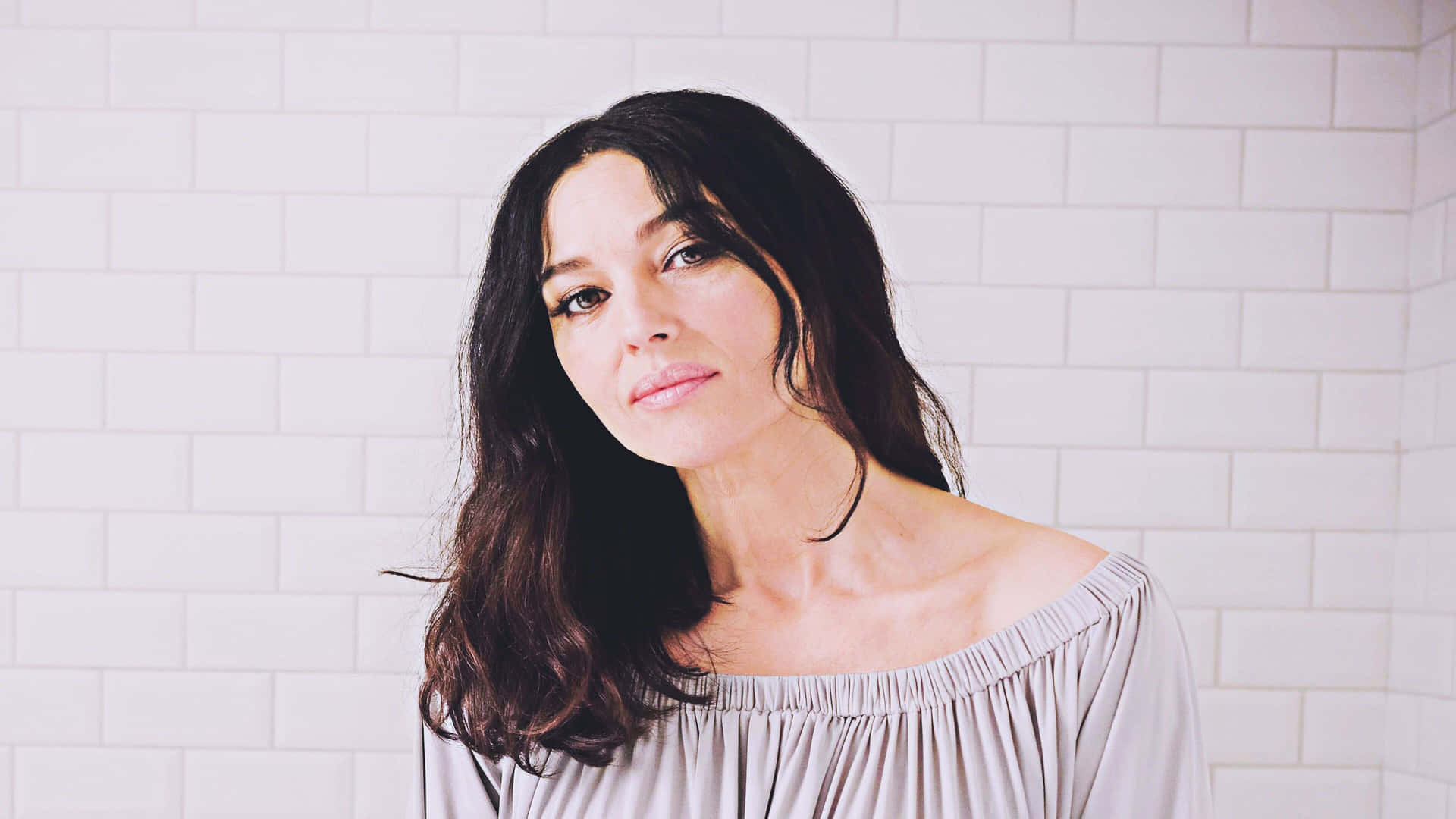 A Woman In A Gray Top Standing In A Bathroom Background