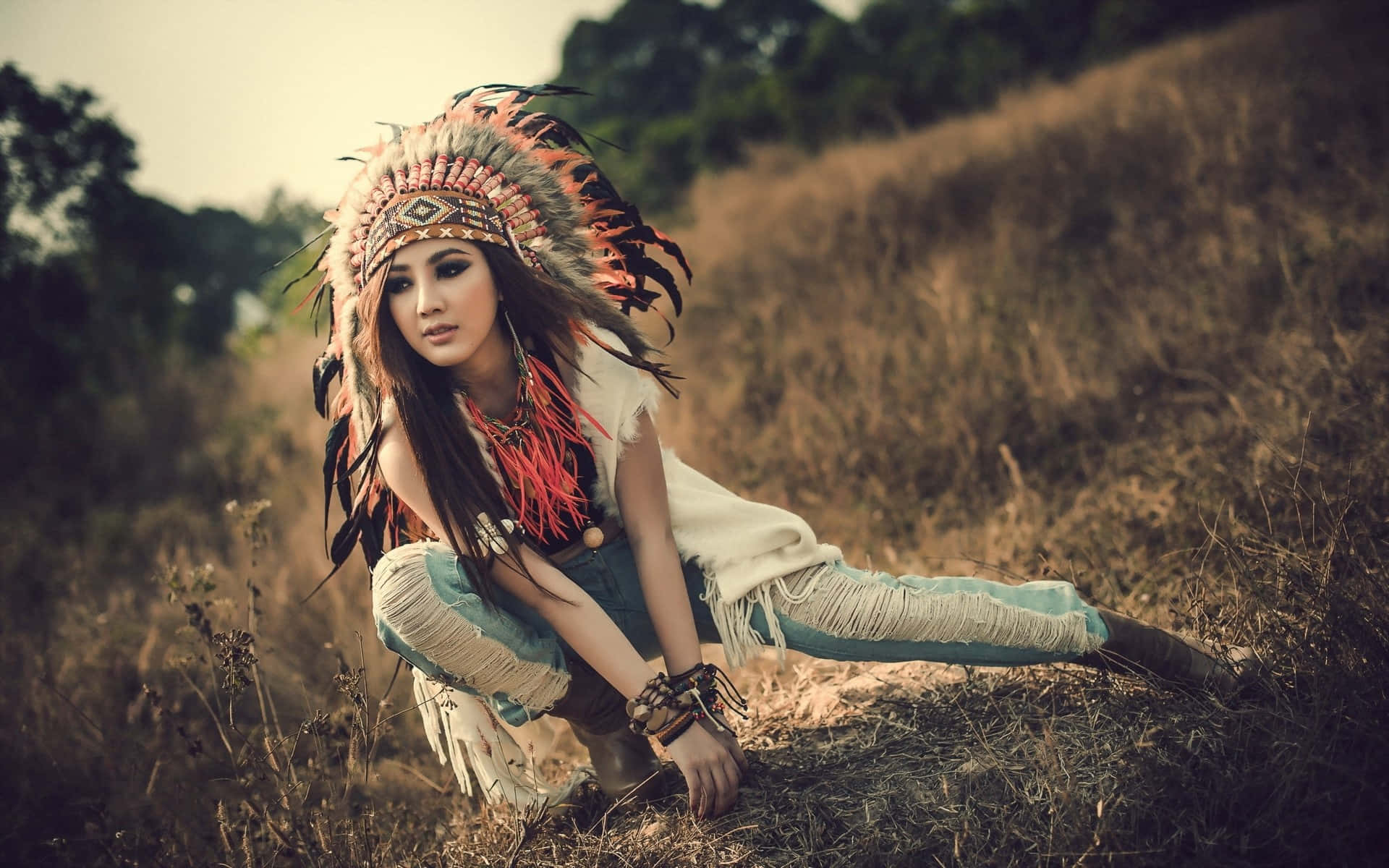 A Woman In A Native American Headdress Posing In A Field Background