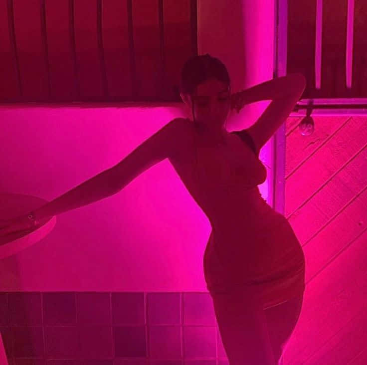 A Woman In A Pink Dress Posing In Front Of A Pink Light Background