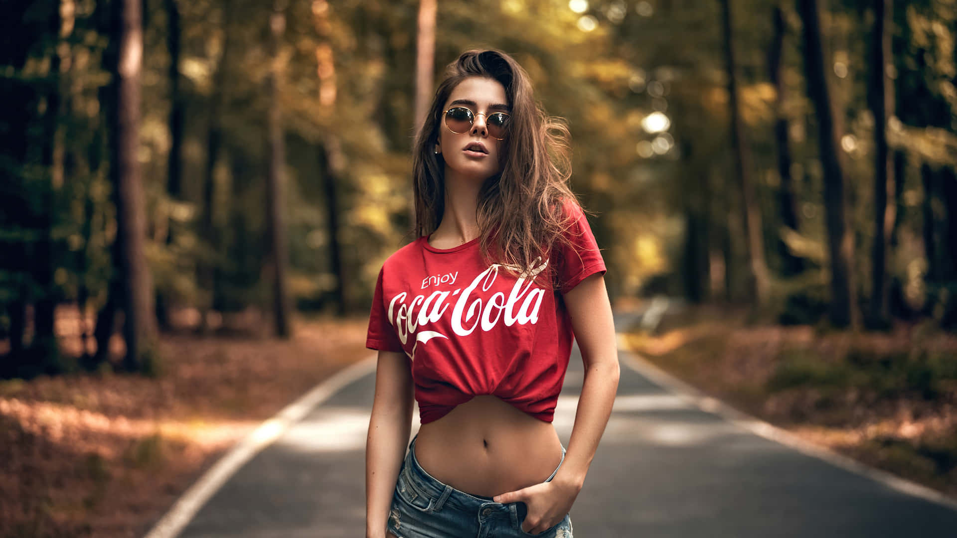 A Woman In A Red Coca Cola Shirt Standing On A Road Background