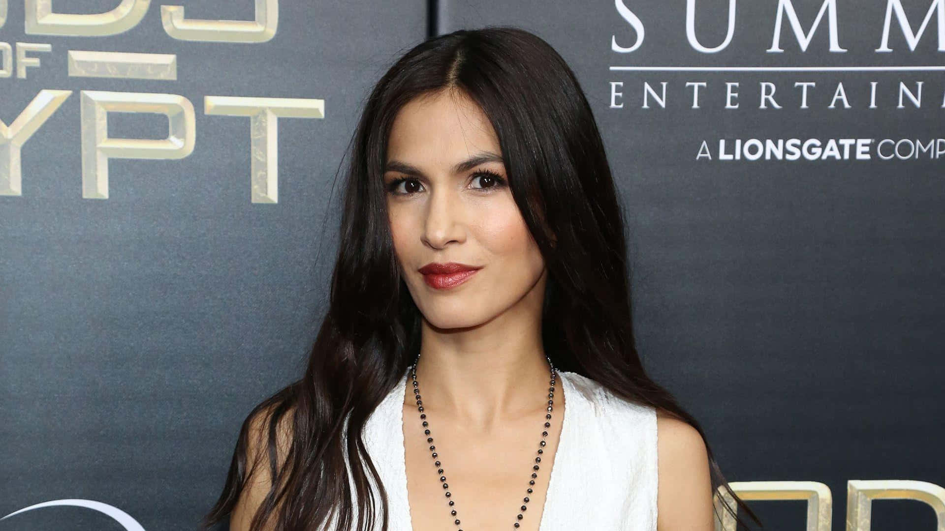 A Woman In A White Dress Is Posing On The Red Carpet Background