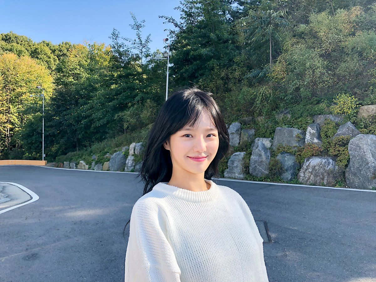 A Woman In A White Sweater Standing In Front Of A Road Background