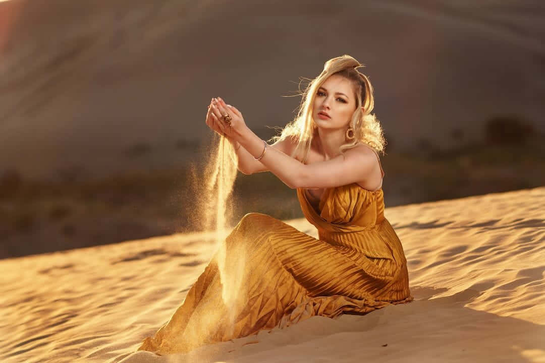 A Woman In A Yellow Dress Is Sitting On A Sand Dune Background