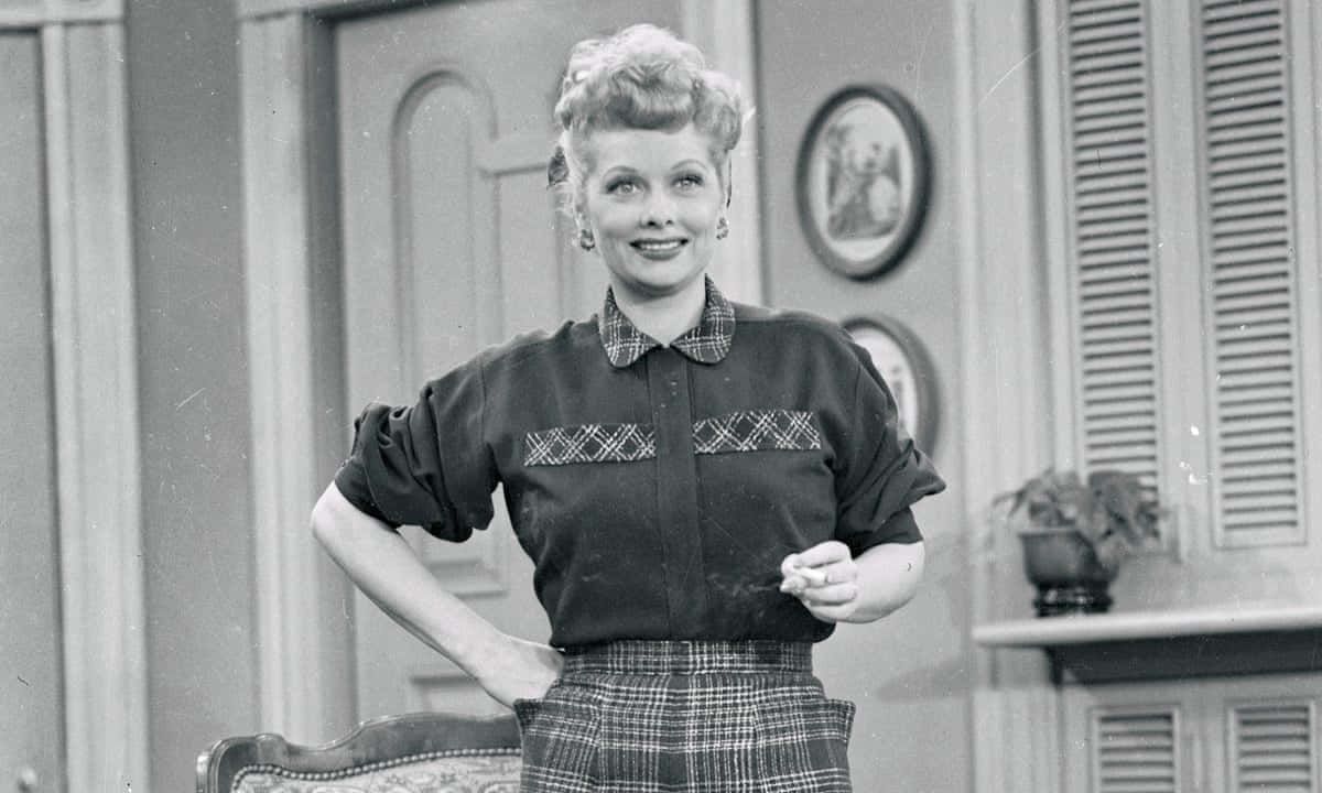A Woman In Plaid Skirt And Shirt Standing In Front Of A Couch