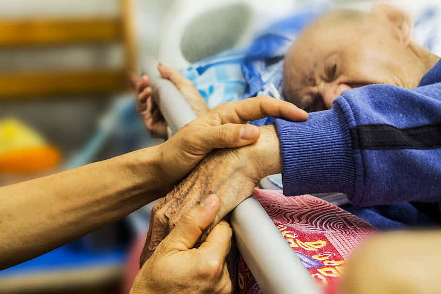 A Woman Is Helping An Elderly Person In A Hospital Bed Background