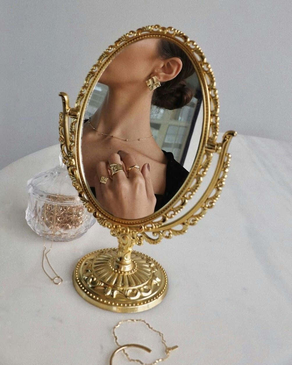 A Woman Is Holding A Gold Mirror And Jewelry Background