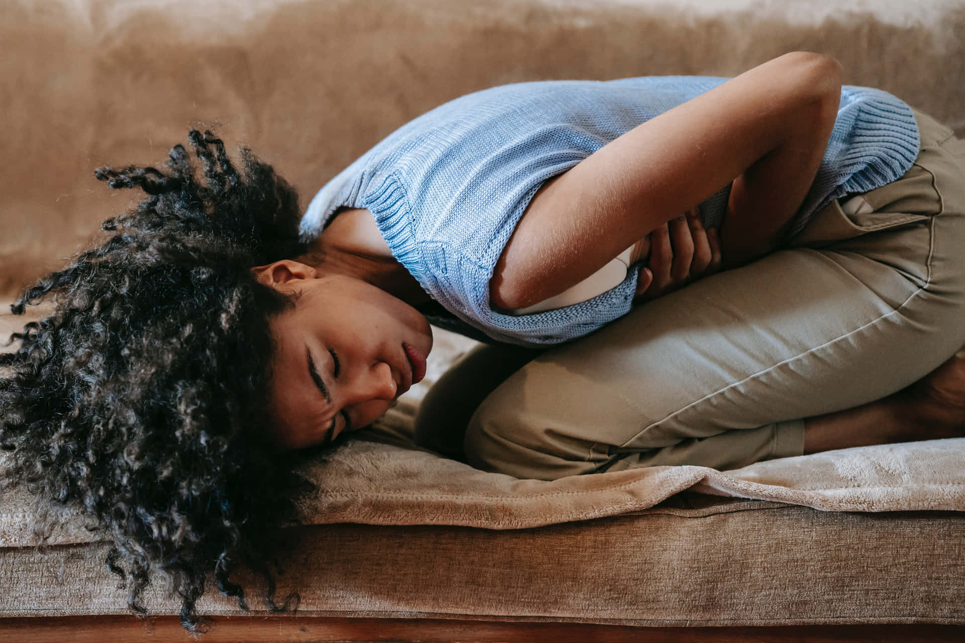 A Woman Is Lying On A Couch With Her Stomach Hurting Background