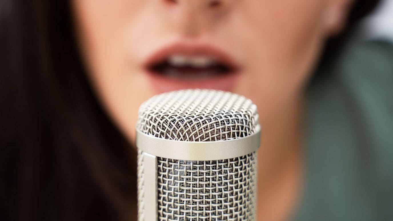 A Woman Is Singing Into A Microphone Background