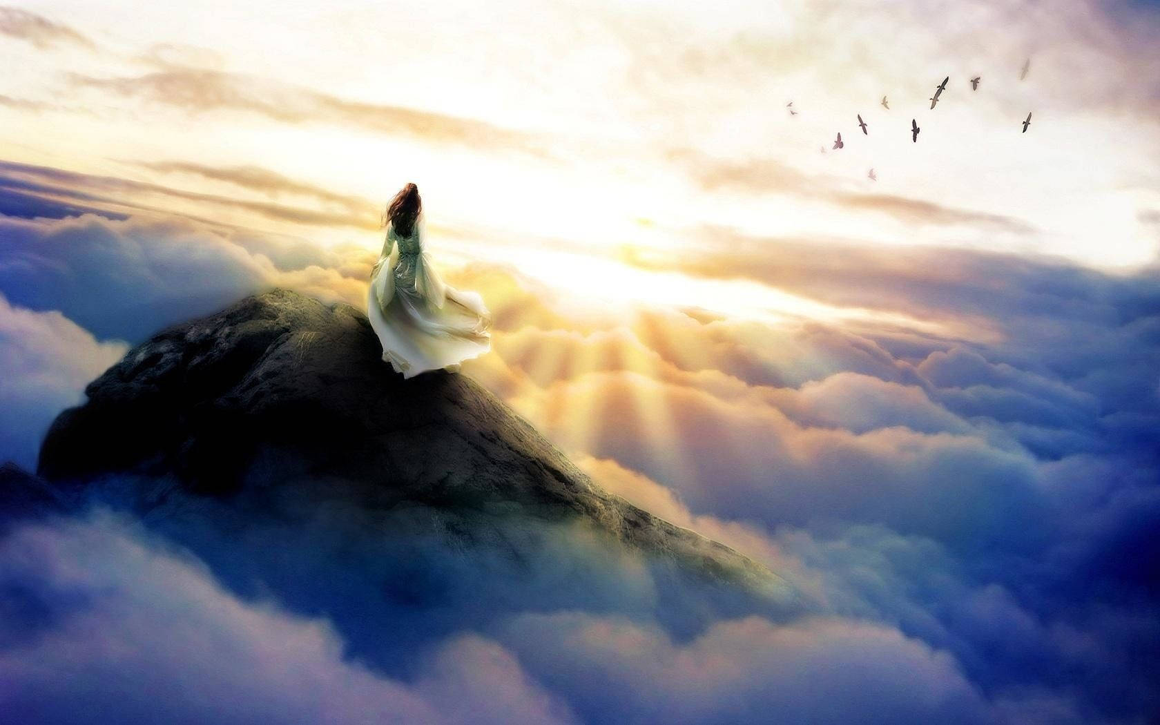 A Woman Is Standing On Top Of A Mountain In The Clouds Background