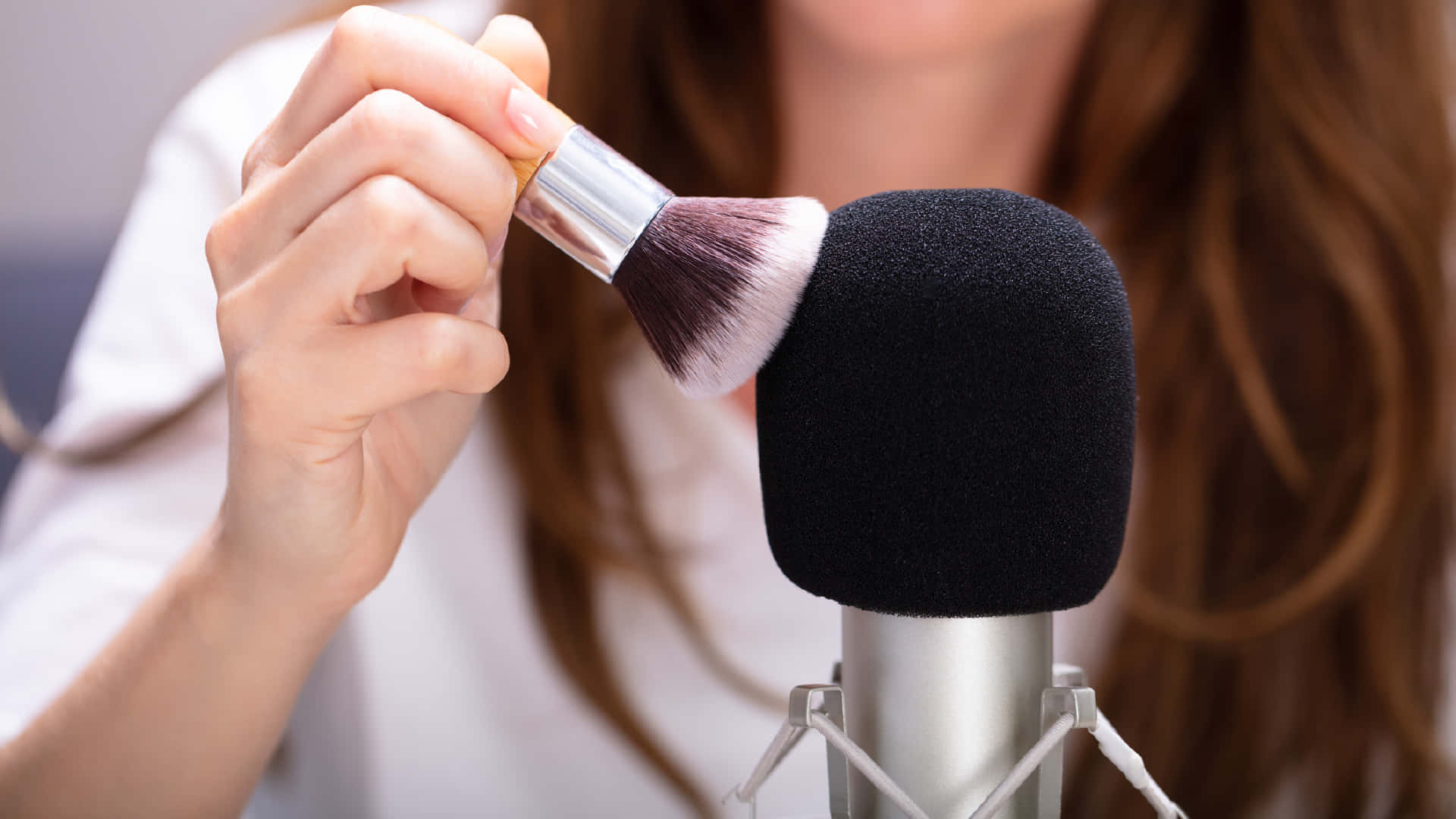 A Woman Is Using A Makeup Brush In Front Of A Microphone Background