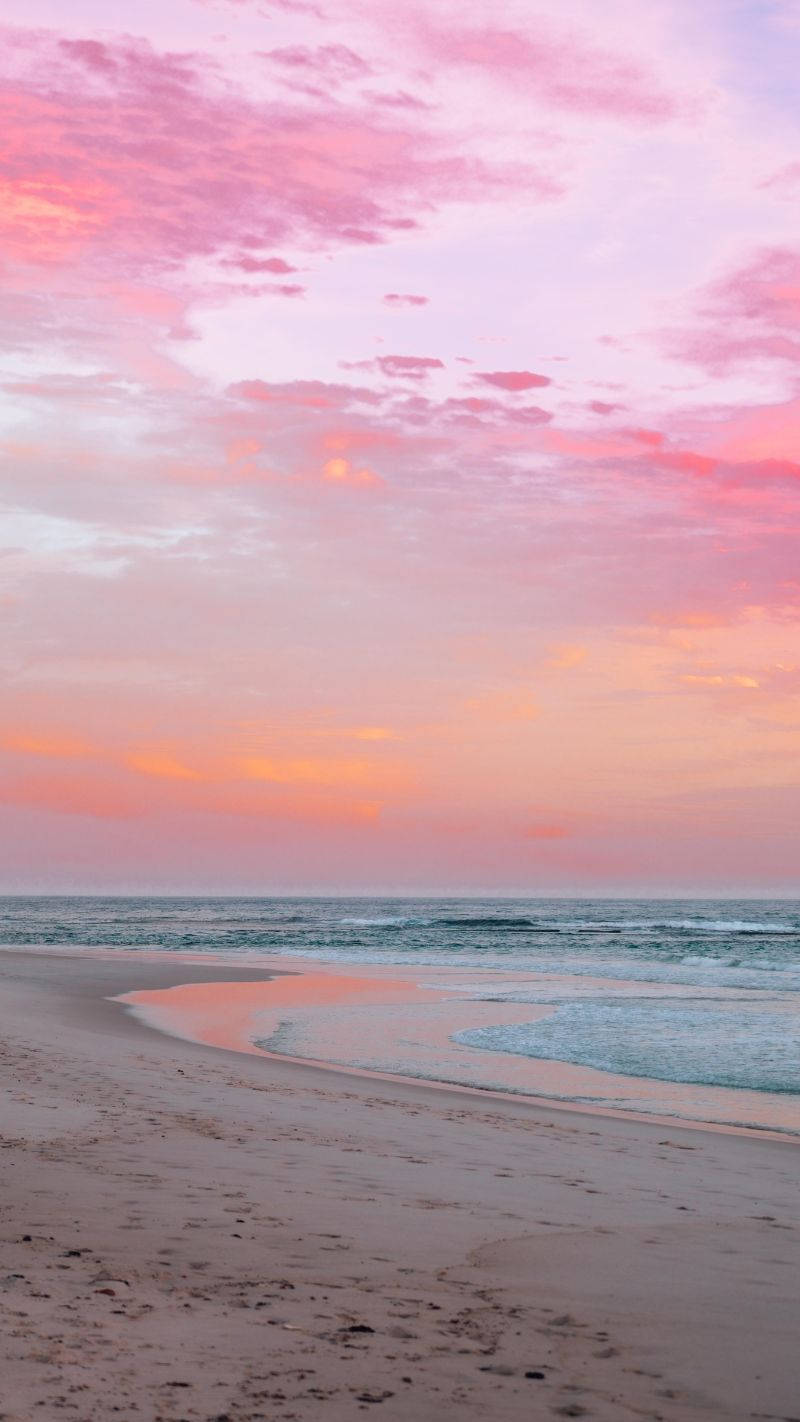 A Woman Is Walking On The Beach At Sunset Background