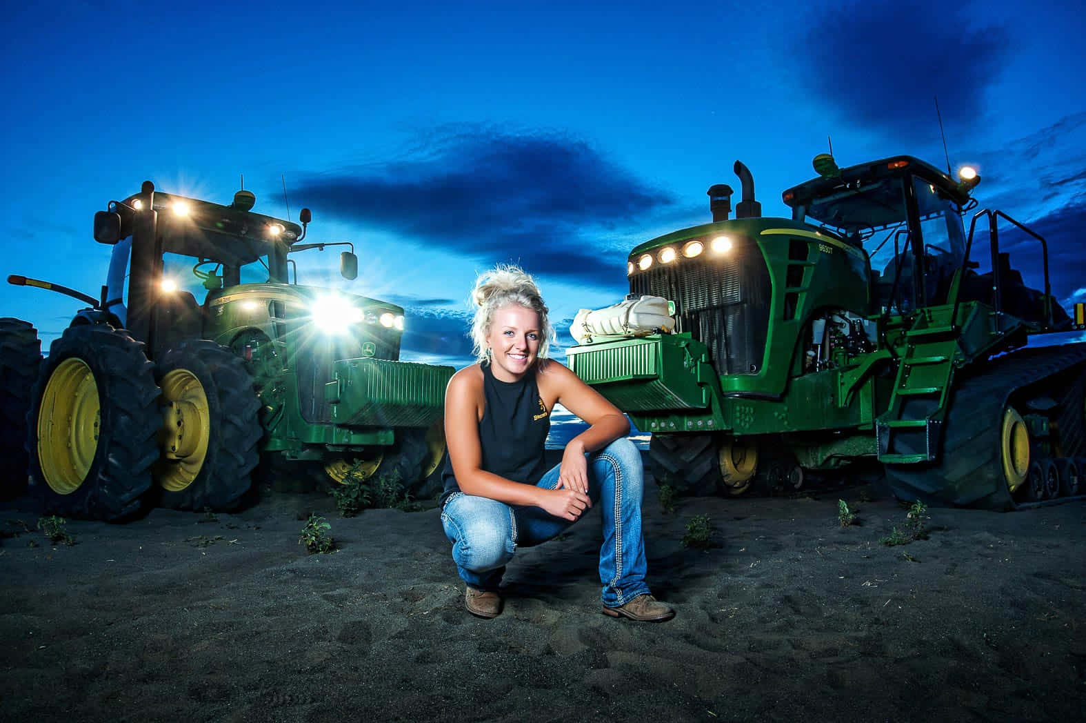 A Woman Kneeling In Front Of Two Tractors Background