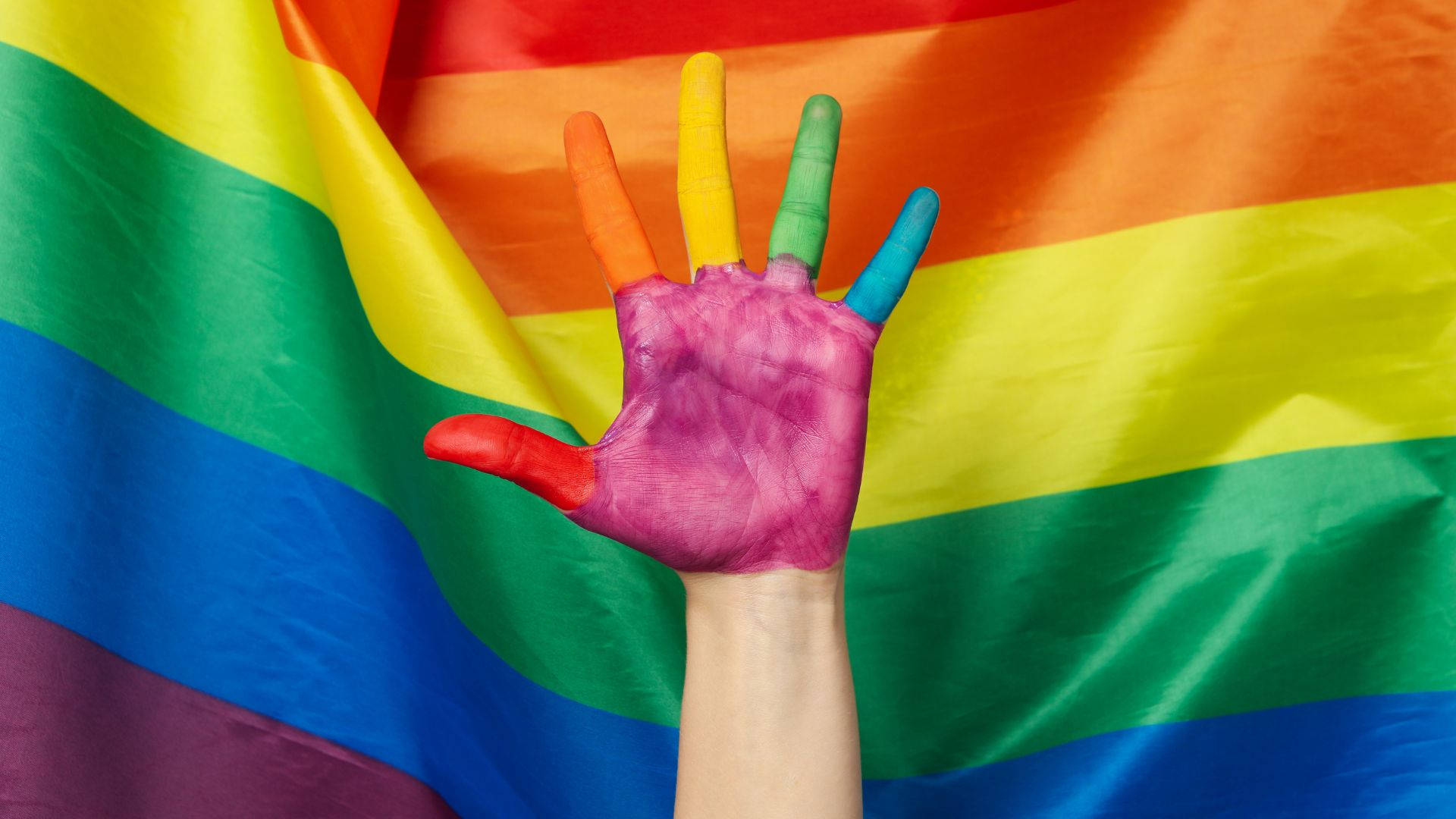 A Woman's Hand Painted With Rainbow Colors Is Raised Up Against A Rainbow Flag