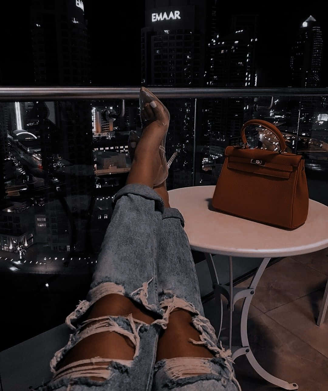 A Woman's Legs On A Table With A Purse And Ripped Jeans Background