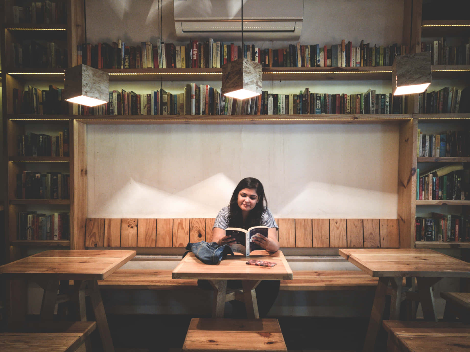A Woman Sitting At A Table Reading A Book Background