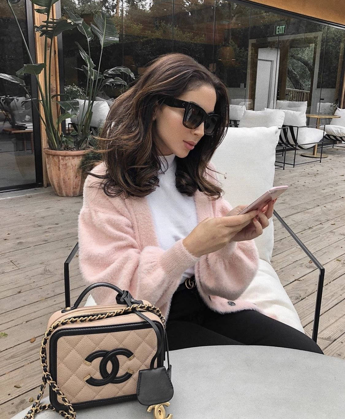 A Woman Sitting On A Bench With A Pink Sweater And Chanel Bag Background