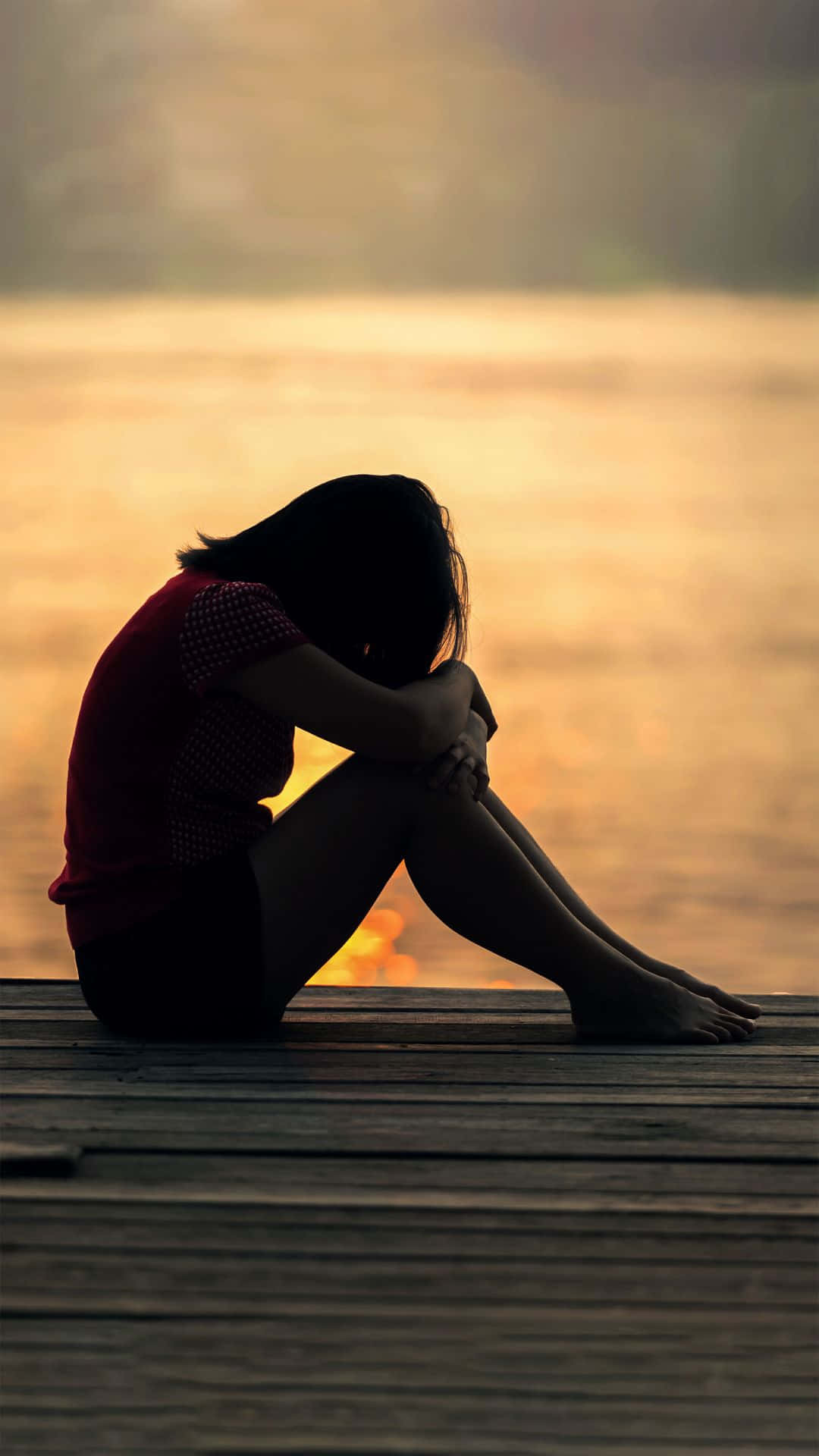 A Woman Sitting On A Dock At Sunset Background