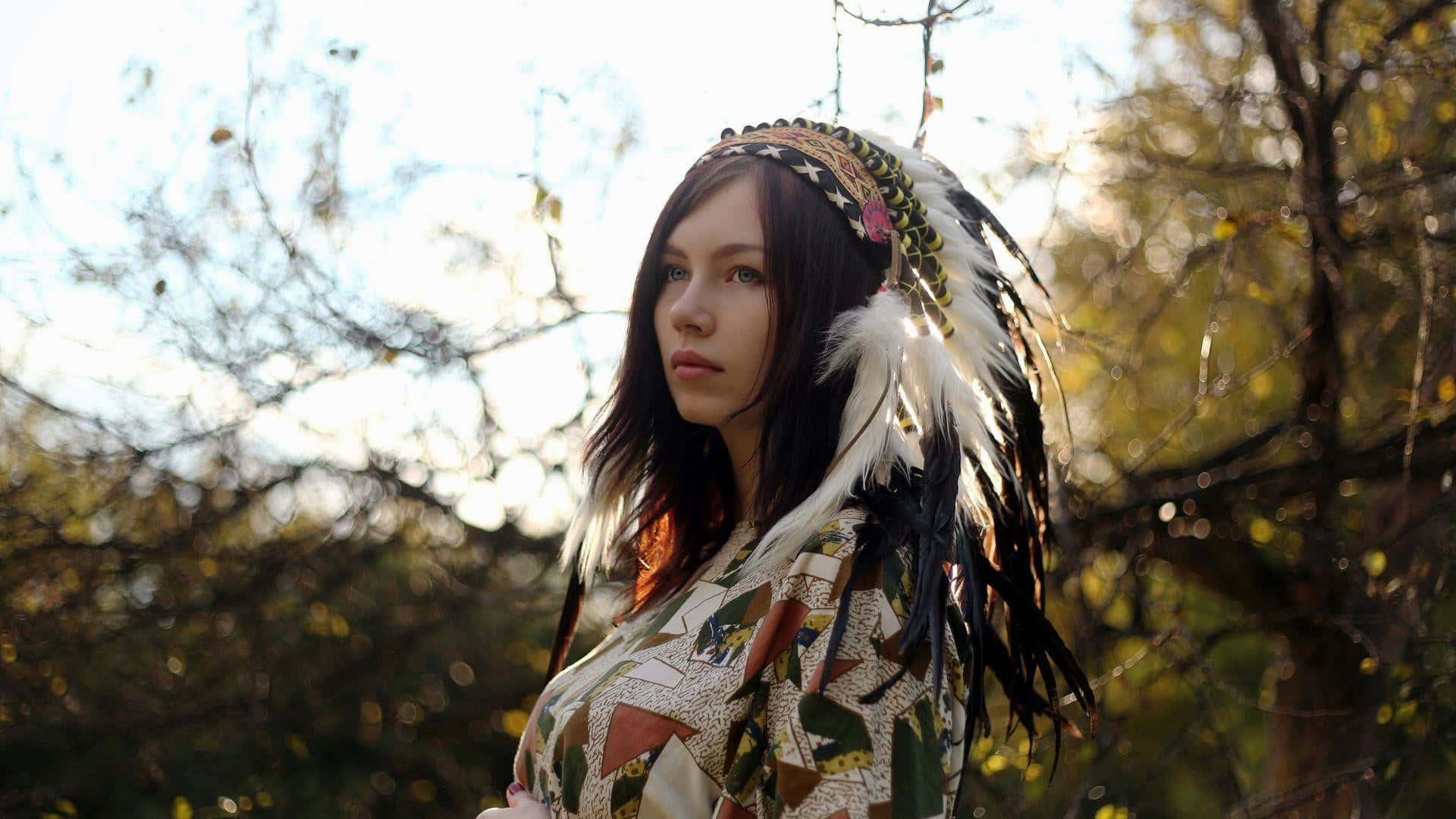 A Woman Wearing A Feathered Headdress In The Forest Background