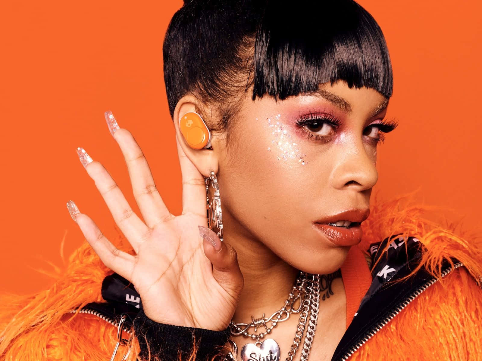 A Woman With Black Hair And Earrings Is Posing With Her Hand On Her Ear Background
