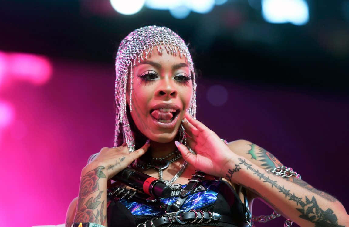 A Woman With Tattoos And A Headdress Is On Stage Background