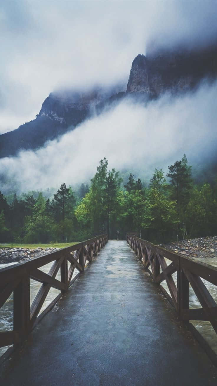 A Wooden Bridge Leading To A Mountain In The Fog Background