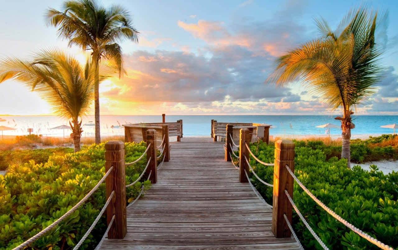 A Wooden Walkway Leading To The Beach At Sunset Background