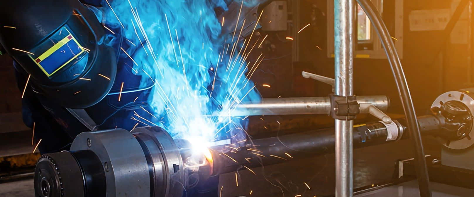 A Worker Is Welding A Metal Pipe With Blue Flames Background